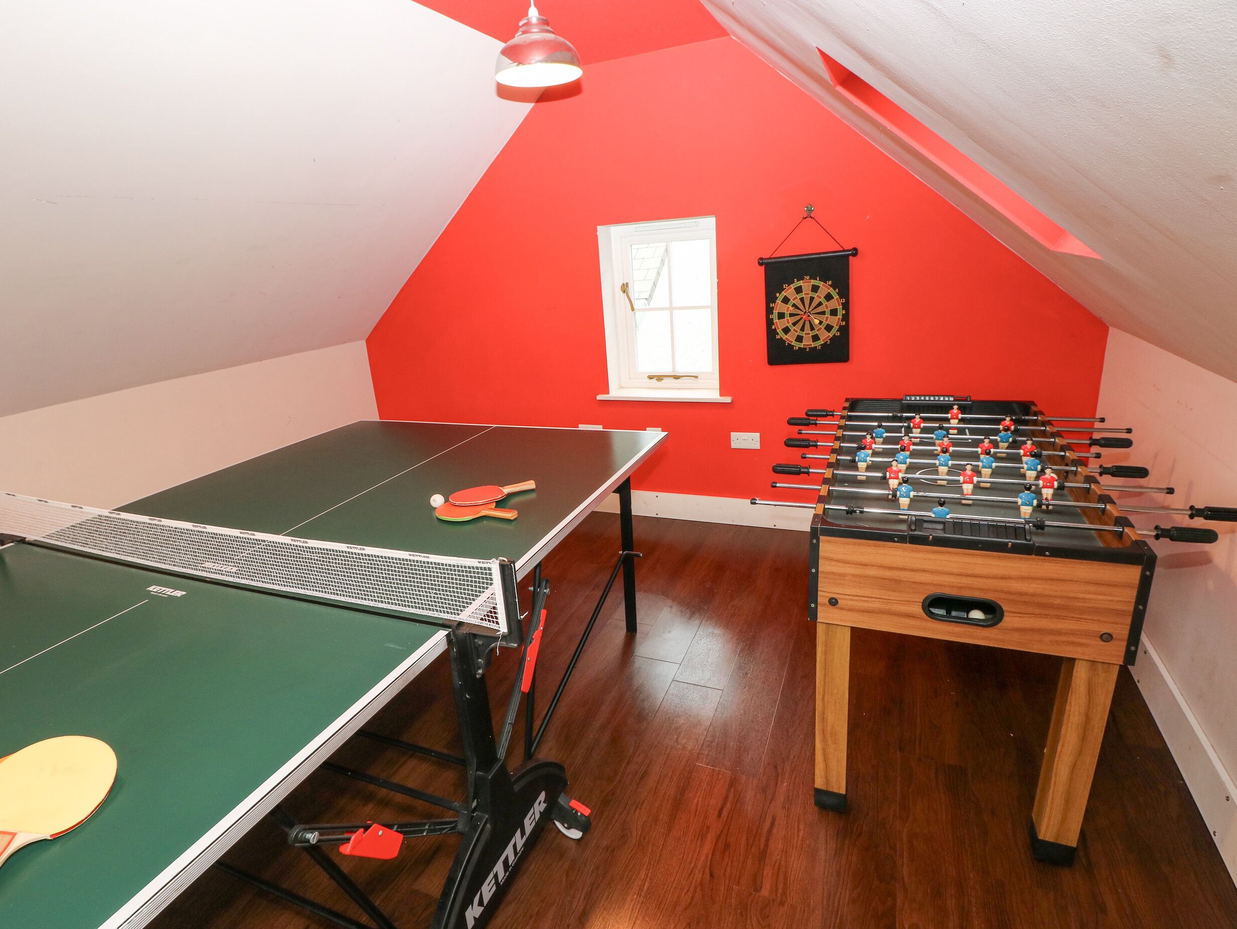 Una habitación con mesa de ping pong, mesa de futbolín y dardos.