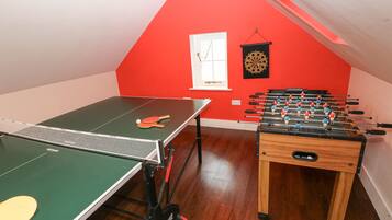 Una habitación con mesa de ping pong, mesa de futbolín y dardos.