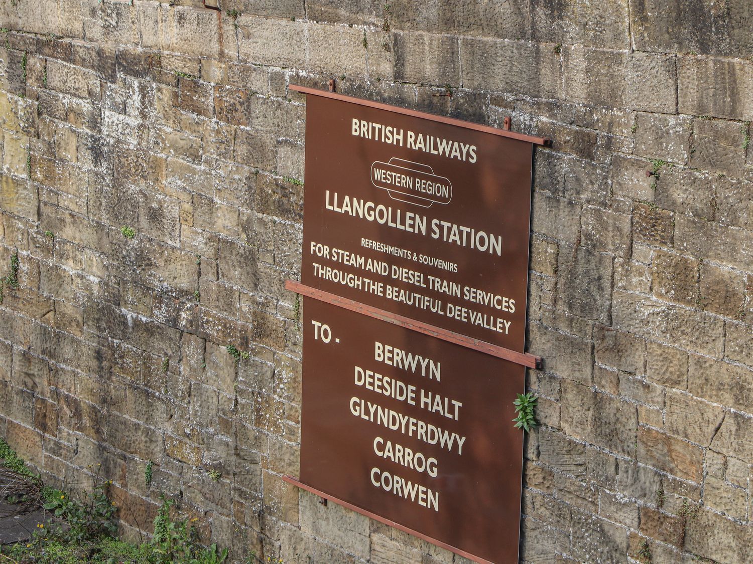 A signboard for British Railways Western Region at Llangeollen Station advertising steam and diesel train services to Berwyn, Deside Halt, Glyndffrydwy, Carrog, and Corwen.