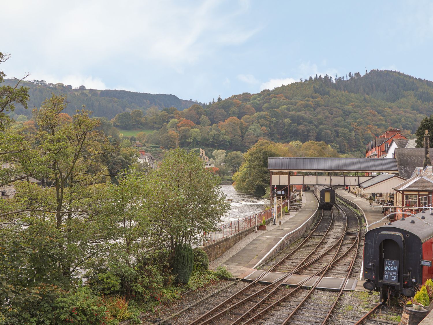A railway station with multiple tracks, a platform, and a building with a sign indicating a tea room.