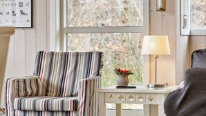 Een gestreepte fauteuil in een kamer met een raam, een tafeltje met een lamp en een decoratieve schaal op het raamkozijn.
