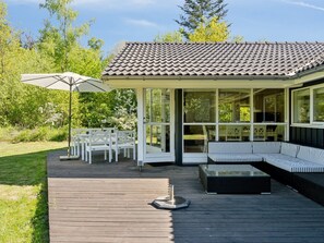 A covered outdoor seating area with a wooden deck, white chairs, and a striped sofa.