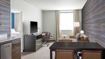 A hotel room with a desk, chair, TV, sofa, and a dining table with chairs.