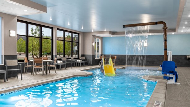 An indoor swimming pool with a water slide, seating area, and large windows. - Residence Inn by Marriott Arvada Denver West (Arvada)