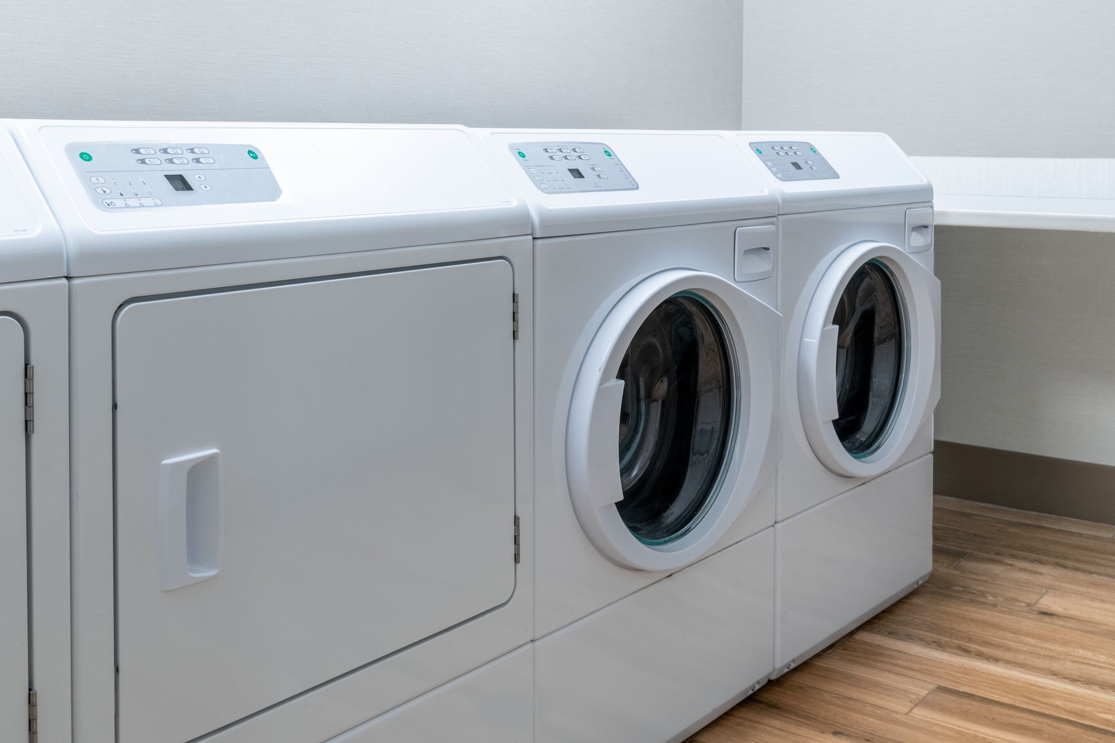 Een rij witte wasmachines met voorlaadopening in een wasserette met houten vloer.