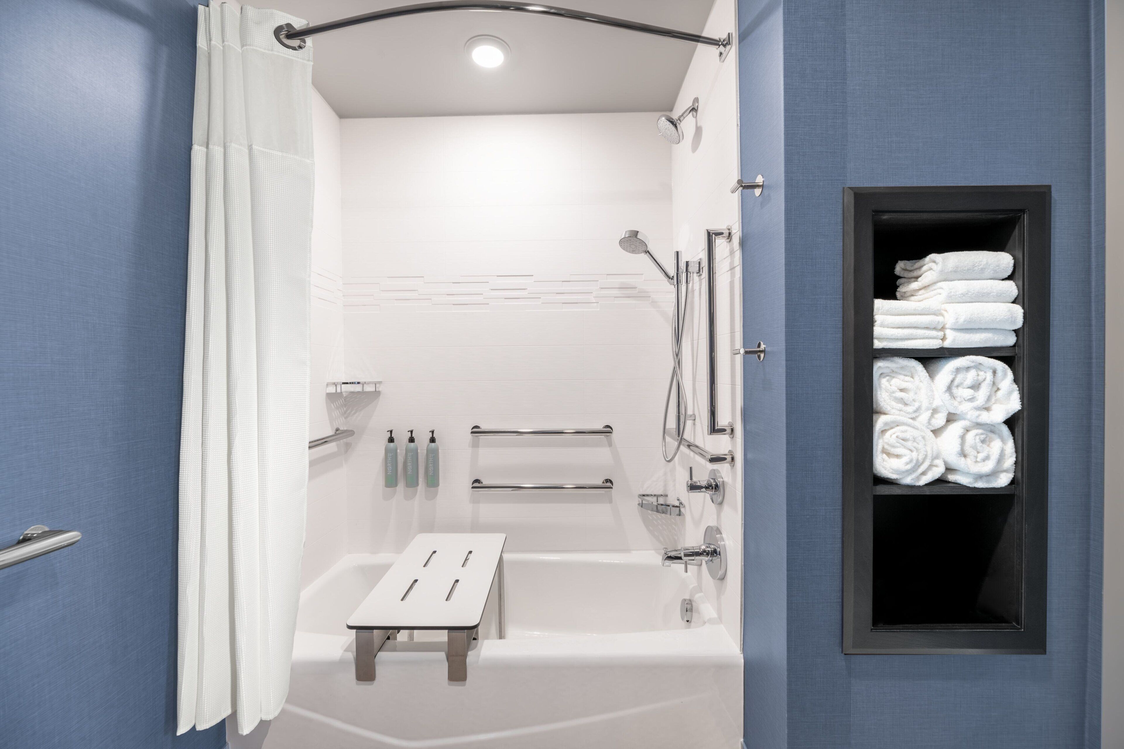 A modern bathroom with a bathtub, shower, and a towel rack with neatly folded towels.