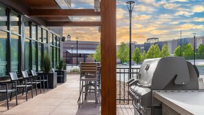 An outdoor patio with a grill, seating area, and a view of a building in the background. - Residence Inn by Marriott Arvada Denver West (Arvada)