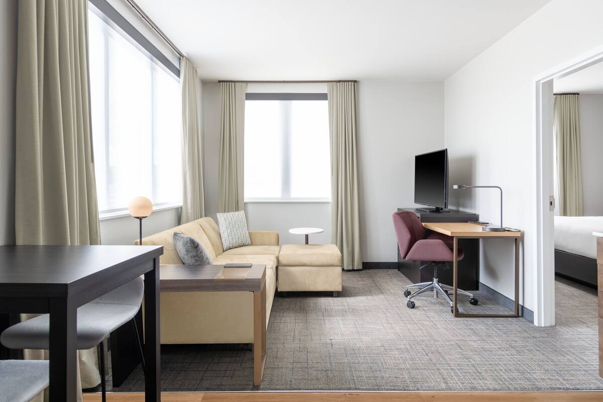 A hotel room with a sofa, a desk, a chair, a TV, and a bed.