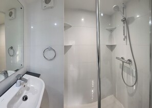 A modern bathroom with a glass-enclosed shower, a sink with a mirror, and two towel rings on the wall.
