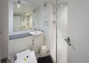 Uma casa de banho moderna com cabine de duche em vidro, uma sanita branca e um espelho em cima.