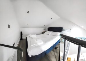 A narrow, single-bed room with a dark headboard, white bedding, and a small bedside table.