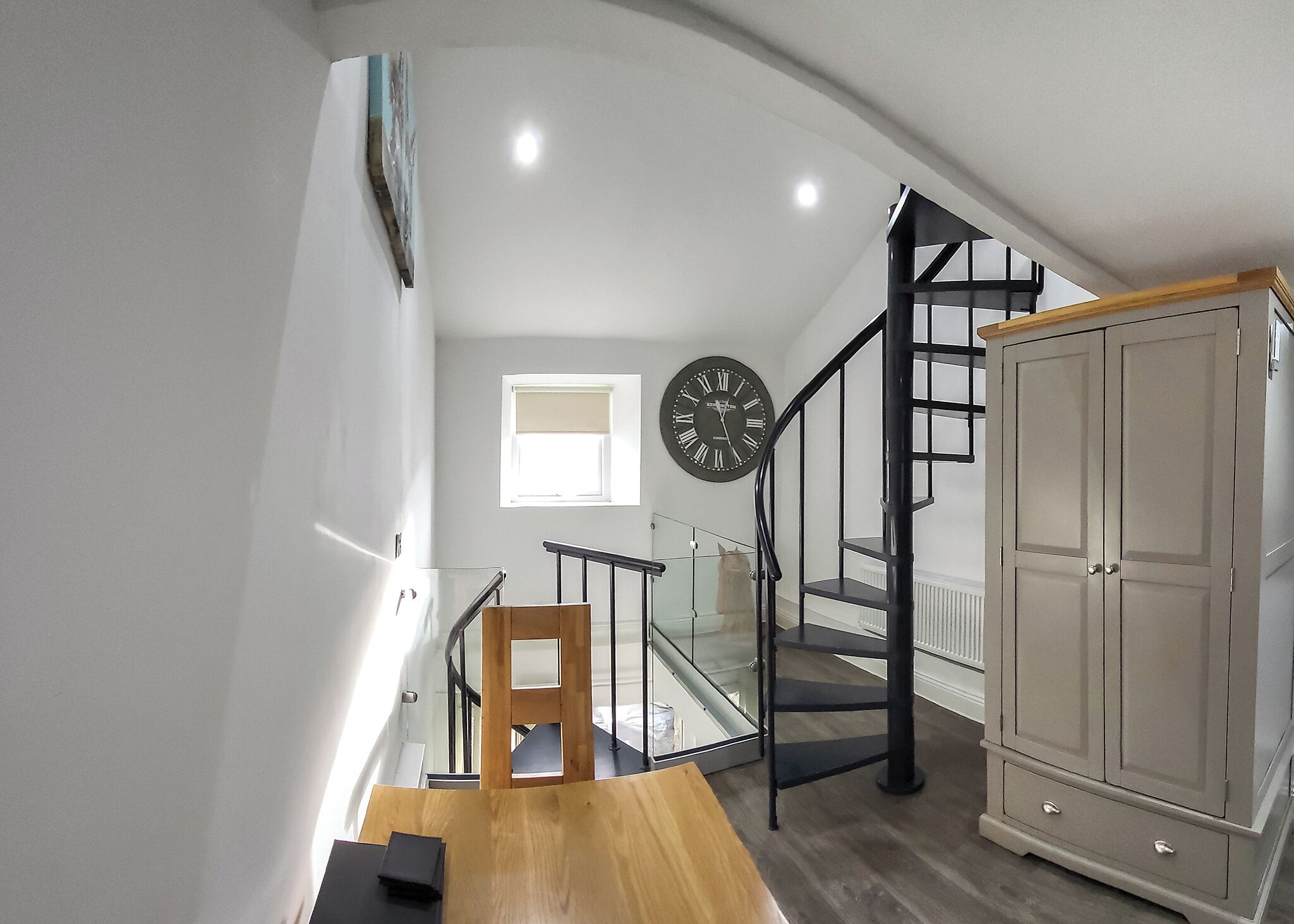 Un escalier avec une rampe en bois, une horloge noire et un meuble.