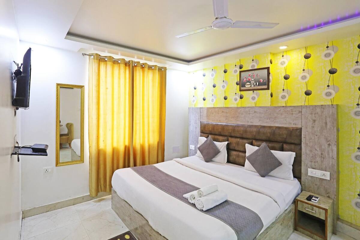 Habitación de hotel con cama, mesita de noche, espejo, televisor y cortina.