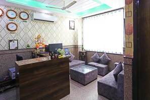 A reception area with a wooden desk, a computer, a statue, and a patterned wall. - Hotel Broadway (New Delhi)
