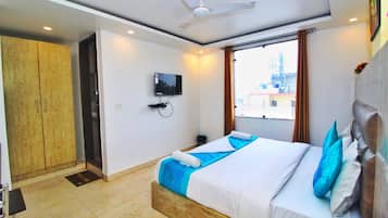 A hotel room with a bed, a television, a ceiling fan, and a window with a view of buildings.