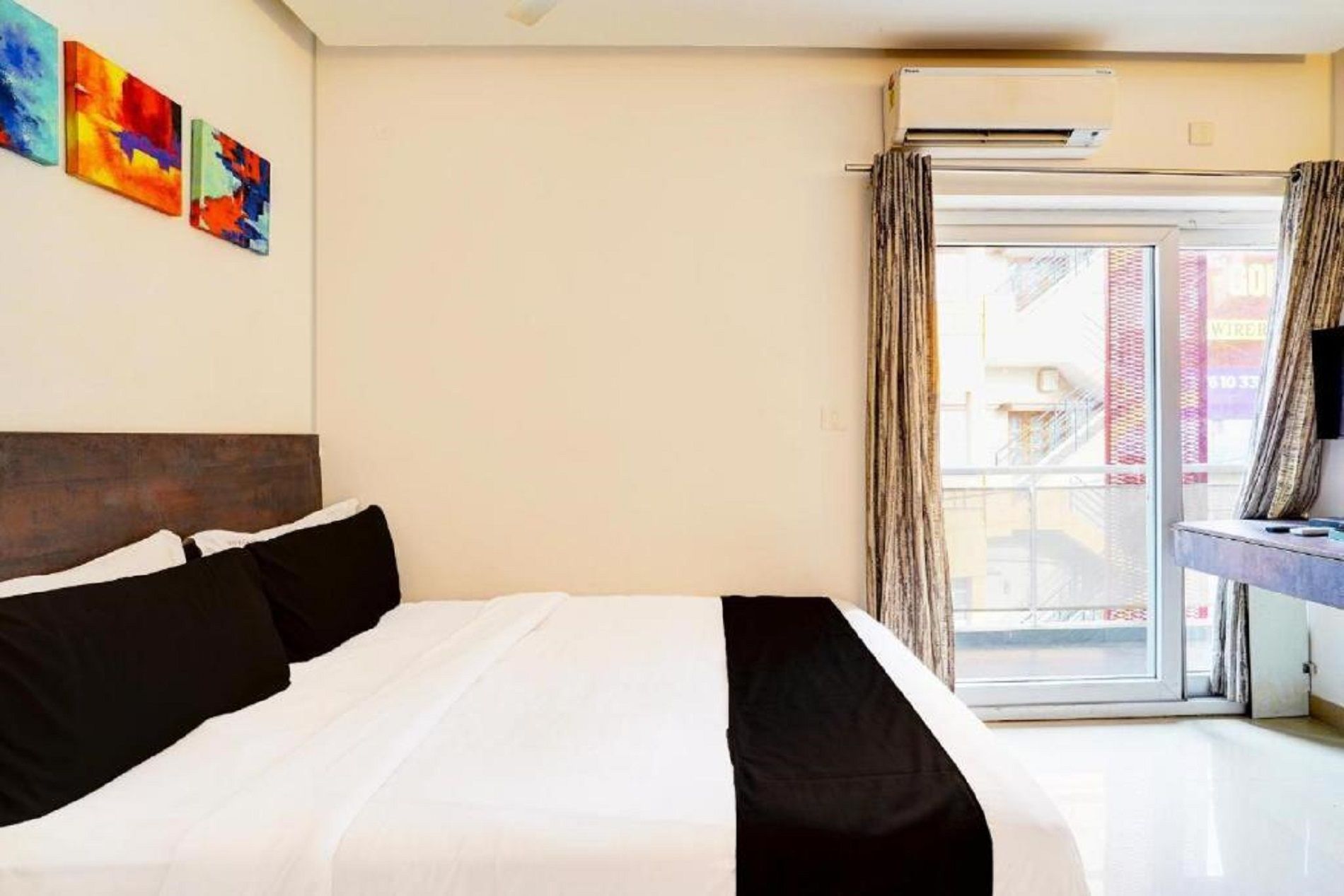 A hotel room with a bed, a window with curtains, and a wall with abstract art.