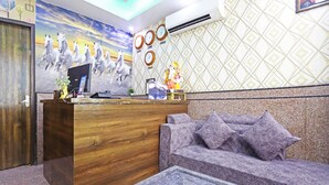 A reception area with a wooden desk, a computer, a sofa, and a small table. - Hotel Broadway (New Delhi)