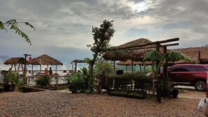 A beachside area with thatched-roof structures, a red vehicle, and a pebbled ground. - Pu Luong May Home & Cafe  (Pu Luong)