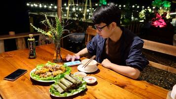 A person dining at an outdoor table with a variety of dishes, a bottle, and a smartphone.