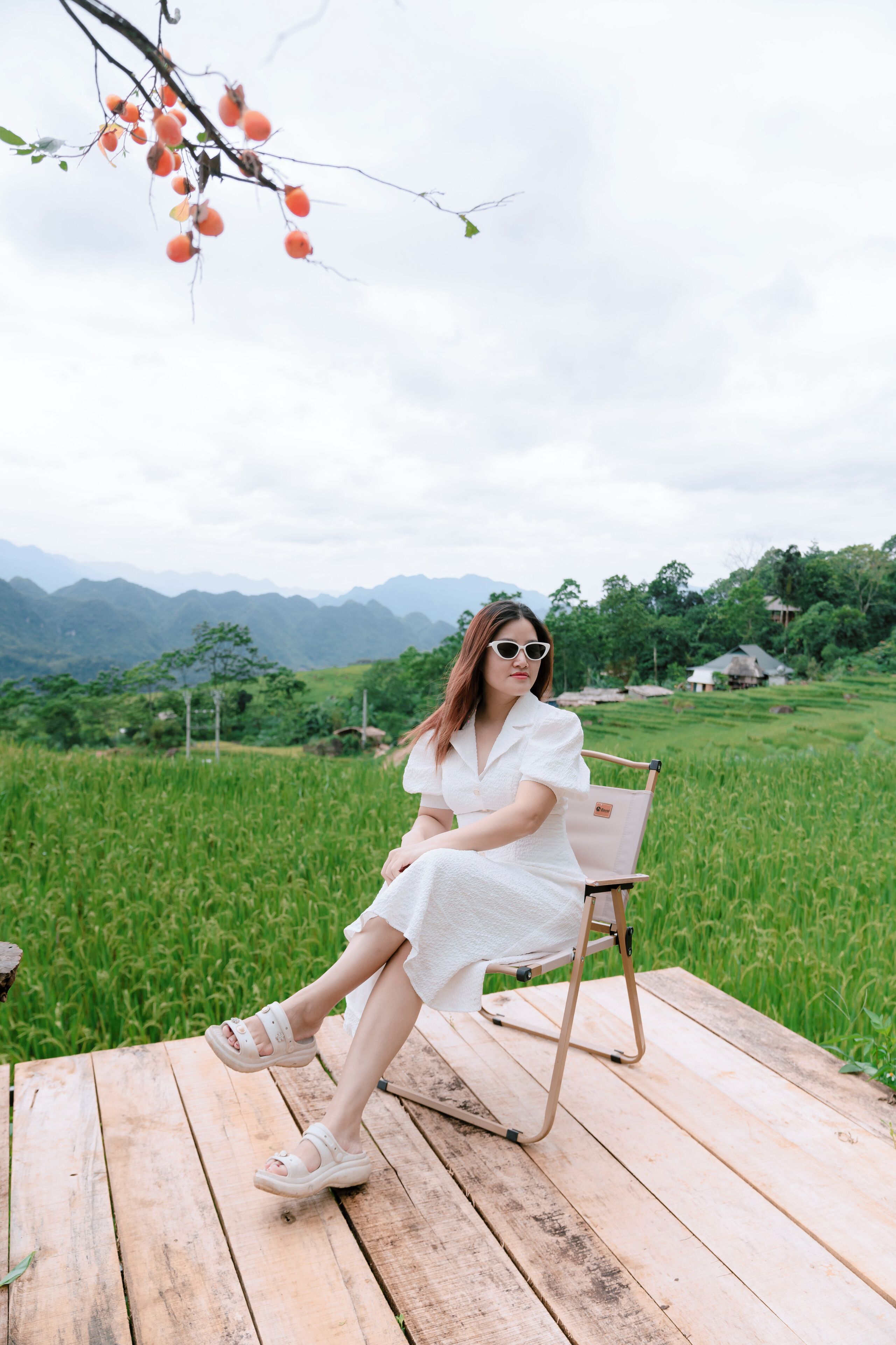 A person sitting on a wooden deck with a view of a green field and mountains in the background.