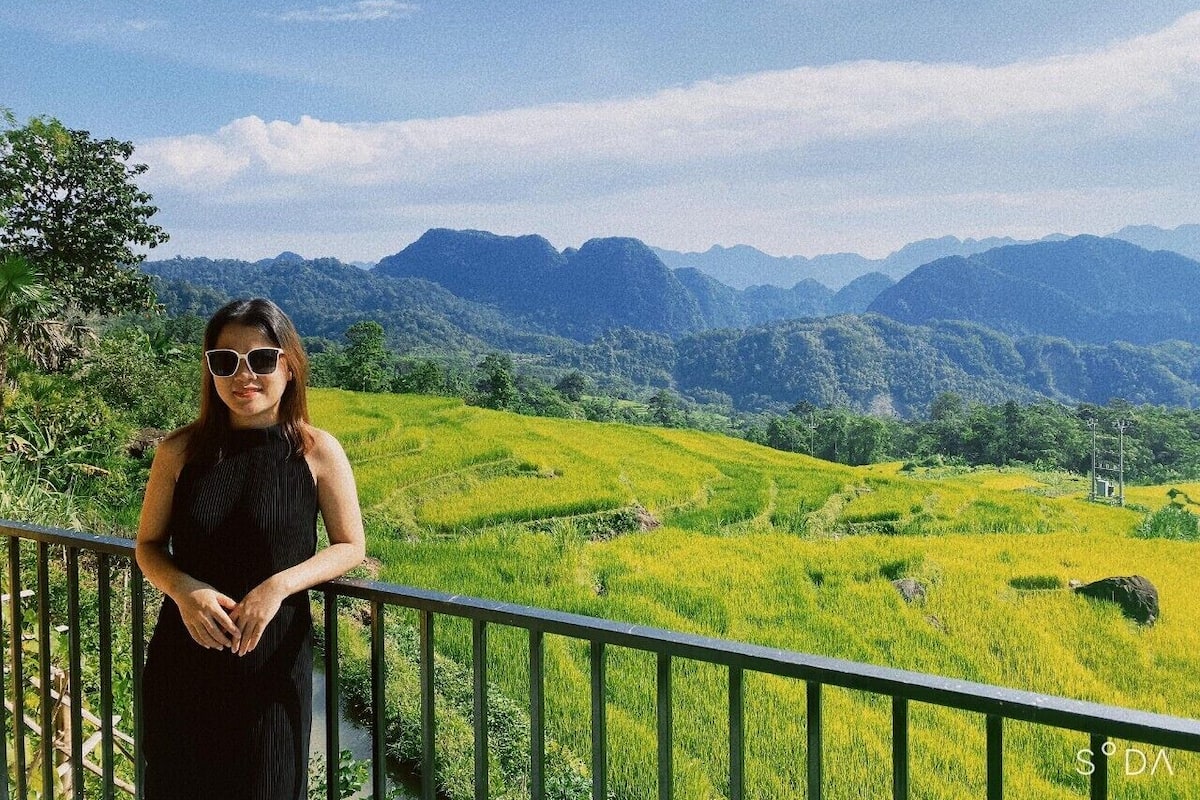 Eine Person steht auf einem Balkon mit Blick auf eine grüne Landschaft und Berge im Hintergrund.