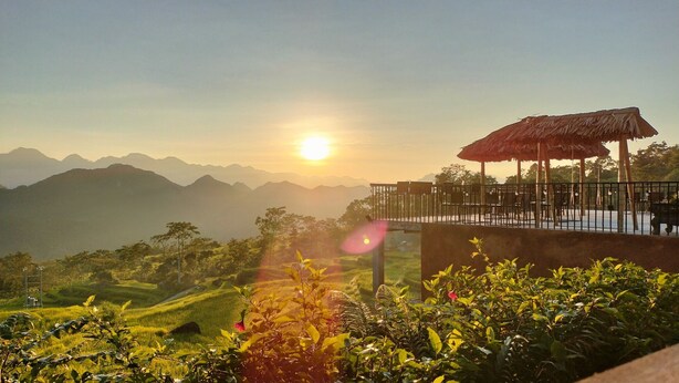 A scenic view of a mountainous landscape with a sunlit sky, a thatched-roof pavilion, and lush greenery. - Pu Luong May Home & Cafe  (Pu Luong)