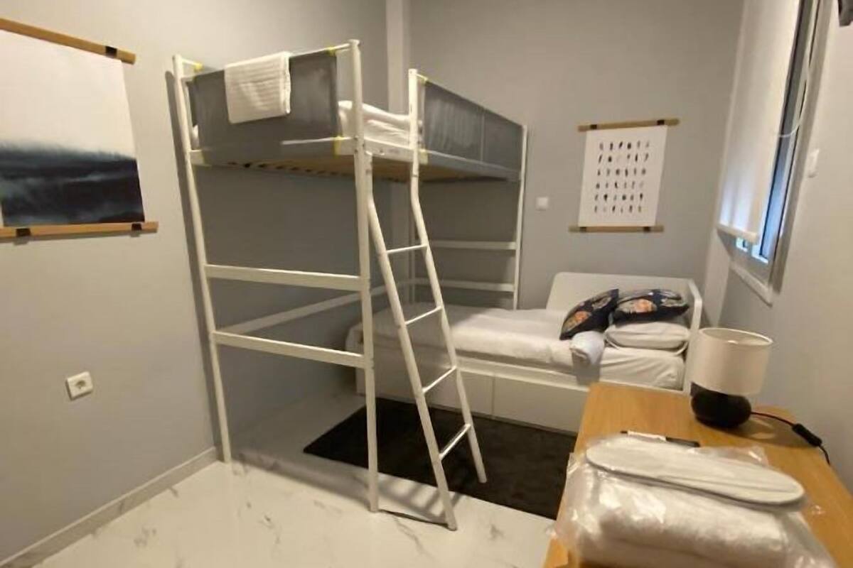 Une chambre avec un lit superposé, une échelle, une table de chevet avec une lampe et un calendrier accroché au mur.