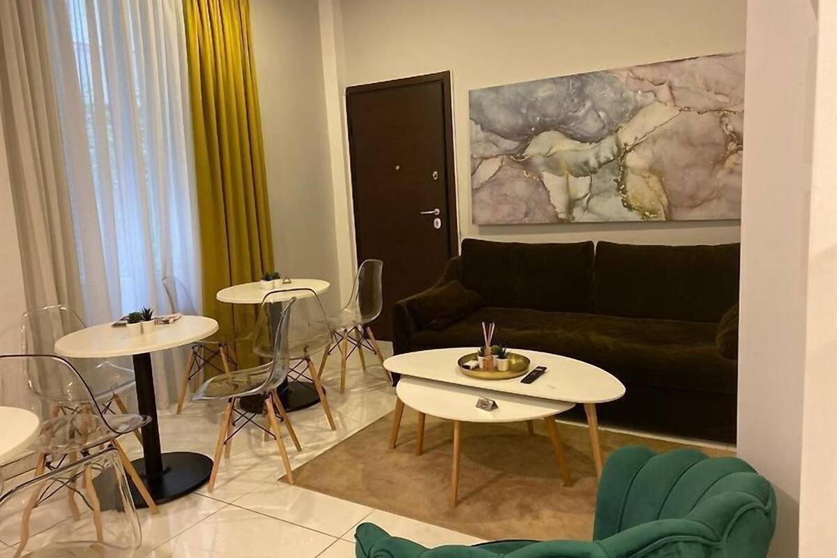 Un salon moderne avec un canapé vert foncé, deux petites tables rondes blanches et un grand tableau abstrait accroché au mur.