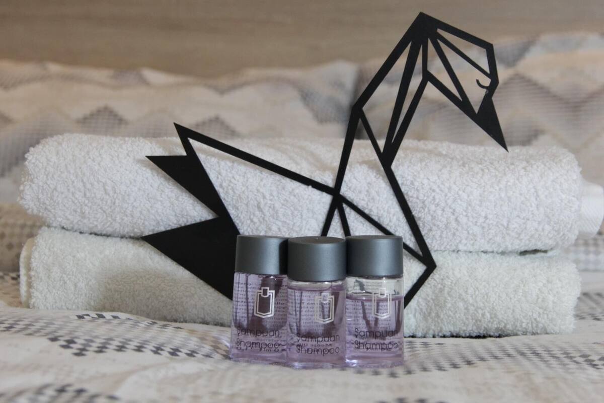 Three bottles of shampoo and three folded towels on a bed with a geometric-patterned blanket.