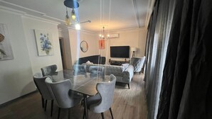 A modern living room with a glass-top dining table, grey upholstered sofas, a flat-screen TV, and a ceiling fan. - Solo Suites Hotel (Istanbul)