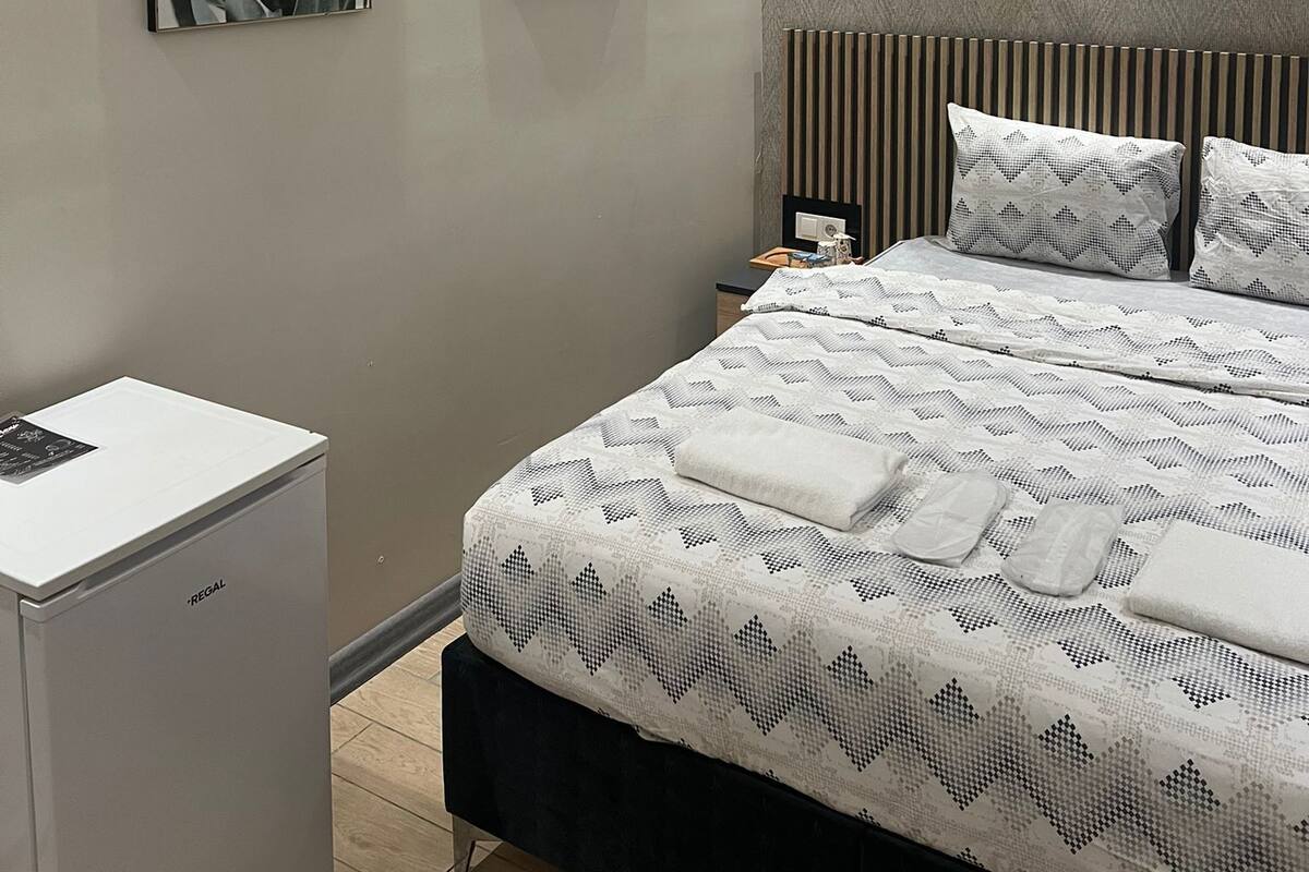 A modern bedroom with a large bed, a bedside table, a nightstand, and a small white cabinet.