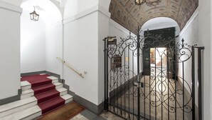 Una escalera con peldaños alfombrados de color rojo que conduce a una habitación con techo decorativo y una reja de hierro forjado.