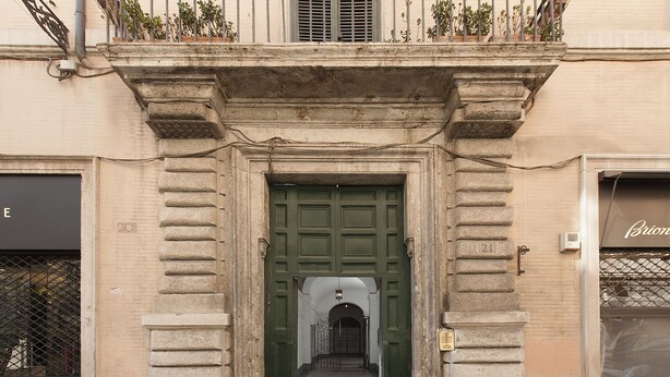 Una entrada de edificio con una puerta verde, un pequeño balcón en lo alto y una escalera que conduce a un nivel superior.