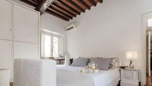 Una cama bien hecha con una bandeja de alimentos para el desayuno, una lámpara de noche y una ventana con cortinas.