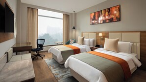 A hotel room with two beds, a desk, a chair, a TV, and a large window with curtains. - Fortune Park, East Delhi - Member ITC Hotels' Group (New Delhi)
