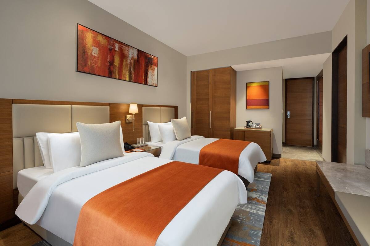 A hotel room with two beds, a large painting, a TV, and a wooden wardrobe.