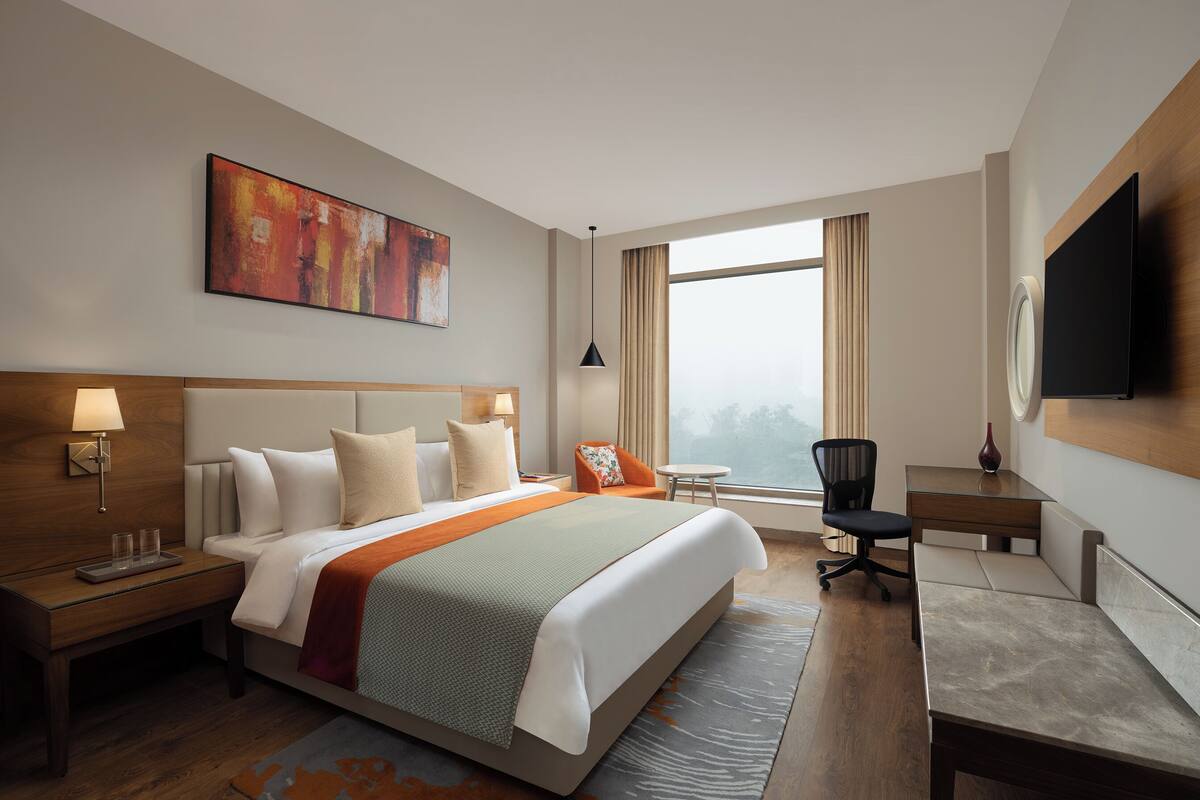 A hotel room with a large bed, a desk, a chair, a TV, and a window with curtains.
