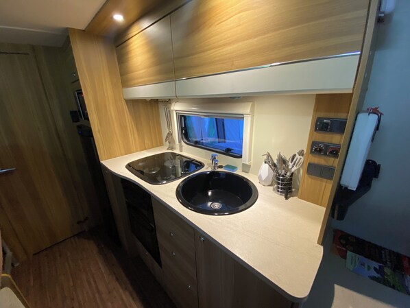 A compact kitchen with a black sink, two stovetops, and a window above the sink. - Rostrevorvalley Caravan Experience Private Hottub (Newry)
