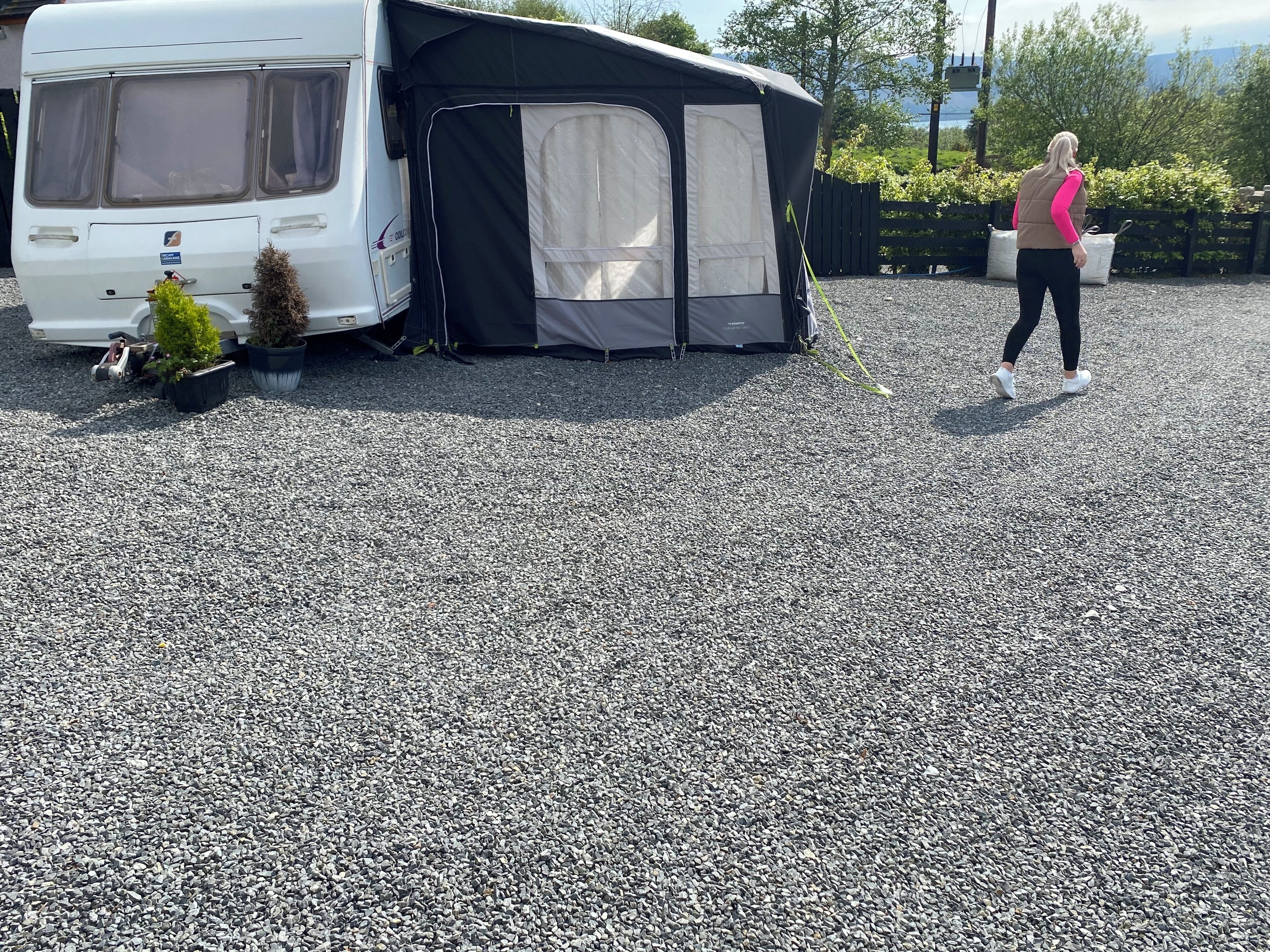 A camping area with a white camper van, a black tent, and a gravel ground.