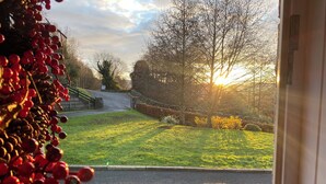 A view through an open door of a paved area with a grassy lawn, a stone wall, and trees. - Rostrevor Valley 6-br, Sleeps 20 w/ Hot Tub & View (Newry)