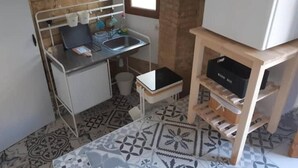 A compact kitchen with a sink, a small refrigerator, and a wooden shelf unit.