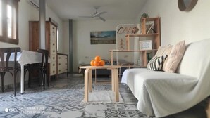 A living room with a sofa, a coffee table with oranges, a bookshelf, and a dining area with chairs and a table.