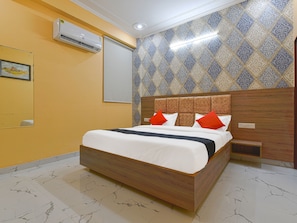 Una habitación de hotel con una cama de madera, una mesita de noche, un equipo de aire acondicionado y papel tapiz estampado.