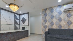 Ein moderner Empfangsbereich mit einer Marmorrezeption, einer Kristallleuchter, einer Wand mit Muster und einem grauen Sofa.