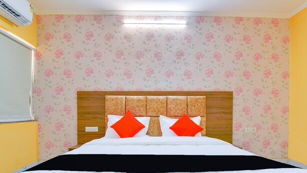 Ein Hotelzimmer mit einem Bett, blumigem Wandpapier, einem Holz-Kopfteil und einem Fenster mit Jalousien.