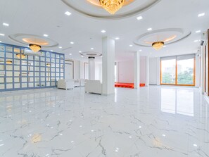 Un vestíbulo espacioso con piso de mármol, sofás blancos, un separador de vidrio azul y candelabros.