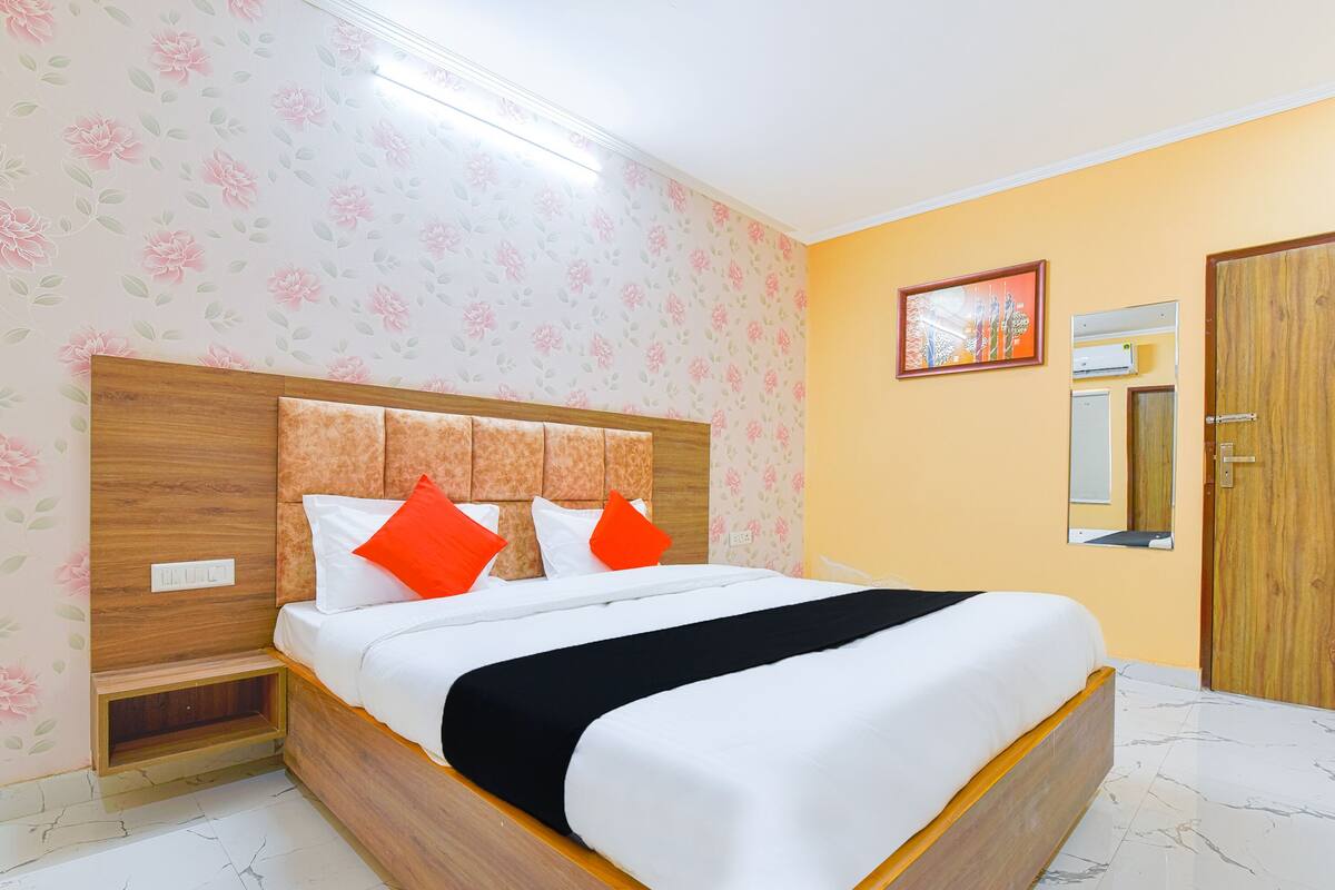 Ein ordentlich gemachtes Bett mit weißer und schwarzer Bettwäsche, einem Holz-Kopfteil und zwei orangen Kissen.