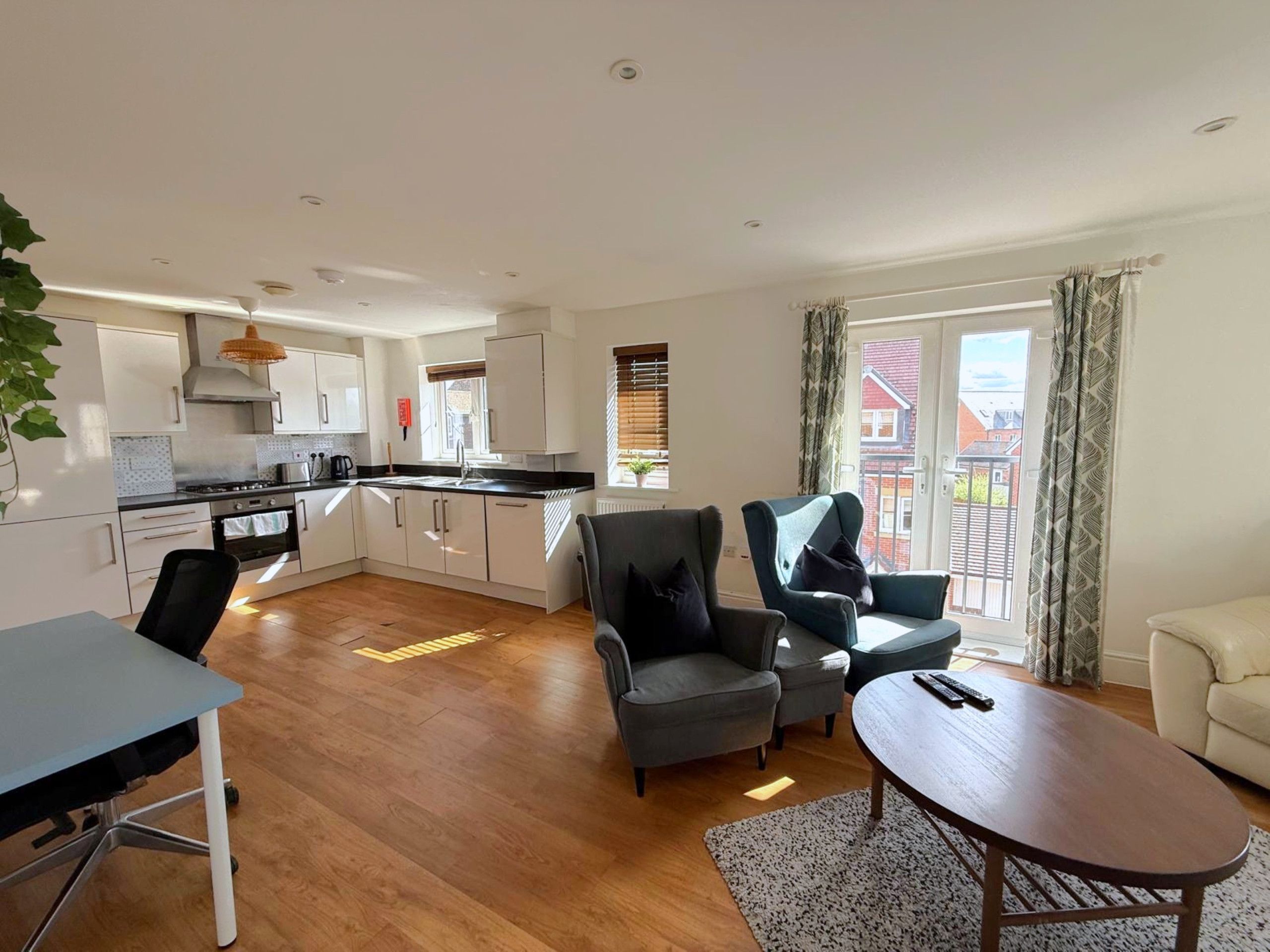 A modern kitchen with white cabinets, a dining table, and a sofa in a living area with a view of a red building.