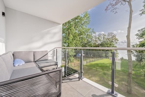 Een balkon met een bank en een kleine tafel, met uitzicht op een grasveld en bomen.