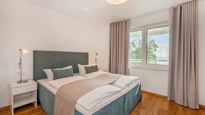 A modern bedroom with a large bed, bedside lamps, a window with curtains, and a view of the outdoors.